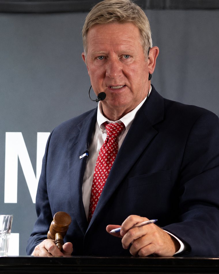 Andrew Miller calling an auction from the rostrum, gavel in hand and headset microphone on